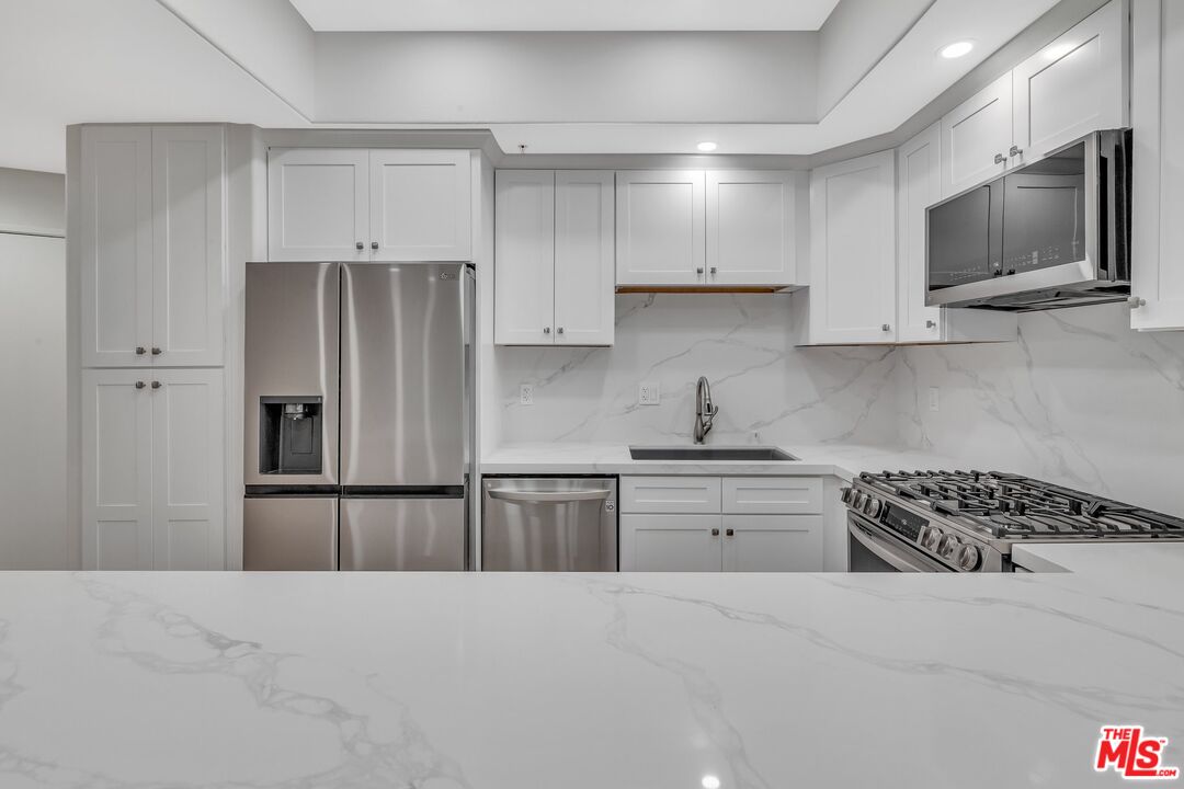 4477 Woodman Avenue, Unit 207 Sherman Oaks, CA 91423 - Photo 3 of 34 a kitchen with granite countertop a refrigerator stove and microwave