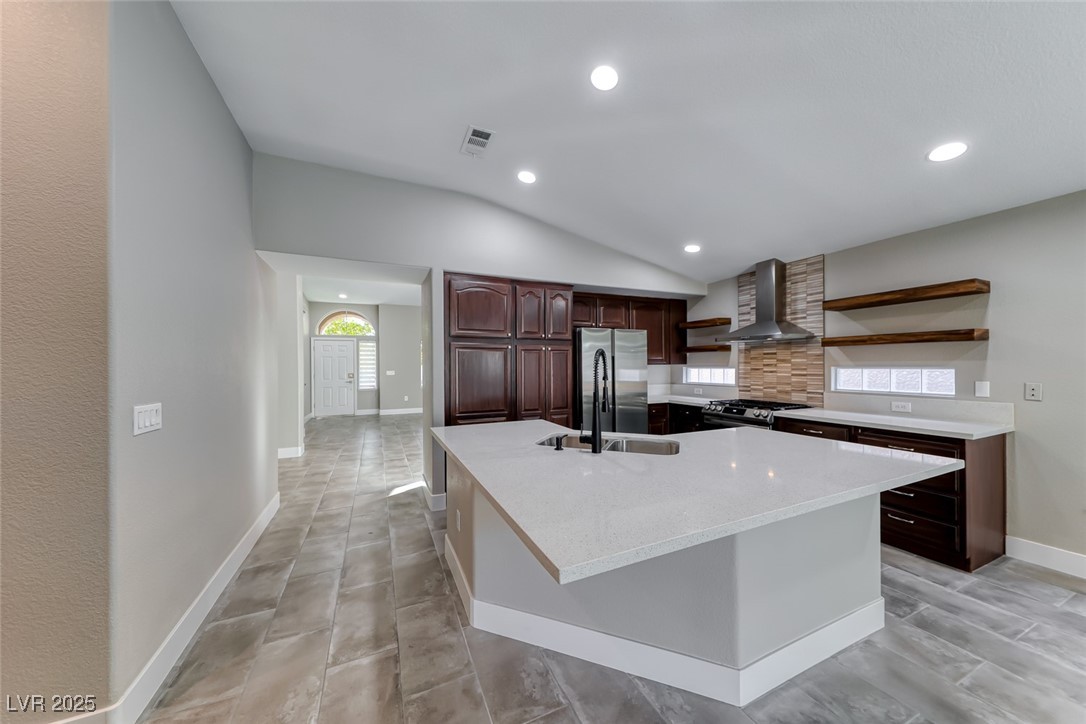 2401 Flower Spring Street Las Vegas, NV 89134 - Photo 12 of 42 Kitchen featuring open shelves, dark brown cabinets, wall chimney range hood, appliances with stainless steel finishes, and a kitchen island with sink