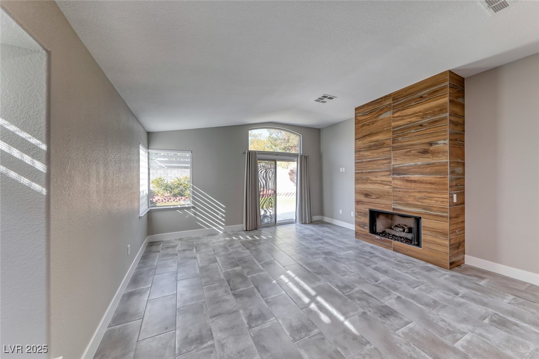 2401 Flower Spring Street Las Vegas, NV 89134 - Photo 13 of 42 Unfurnished living room featuring a tile fireplace, vaulted ceiling, wood finish floors, and a textured wall