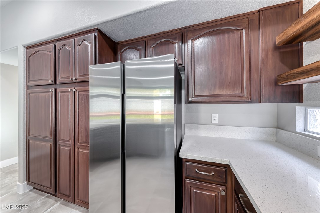2401 Flower Spring Street Las Vegas, NV 89134 - Photo 16 of 42 Kitchen featuring freestanding refrigerator, light stone counters, open shelves, and dark brown cabinetry