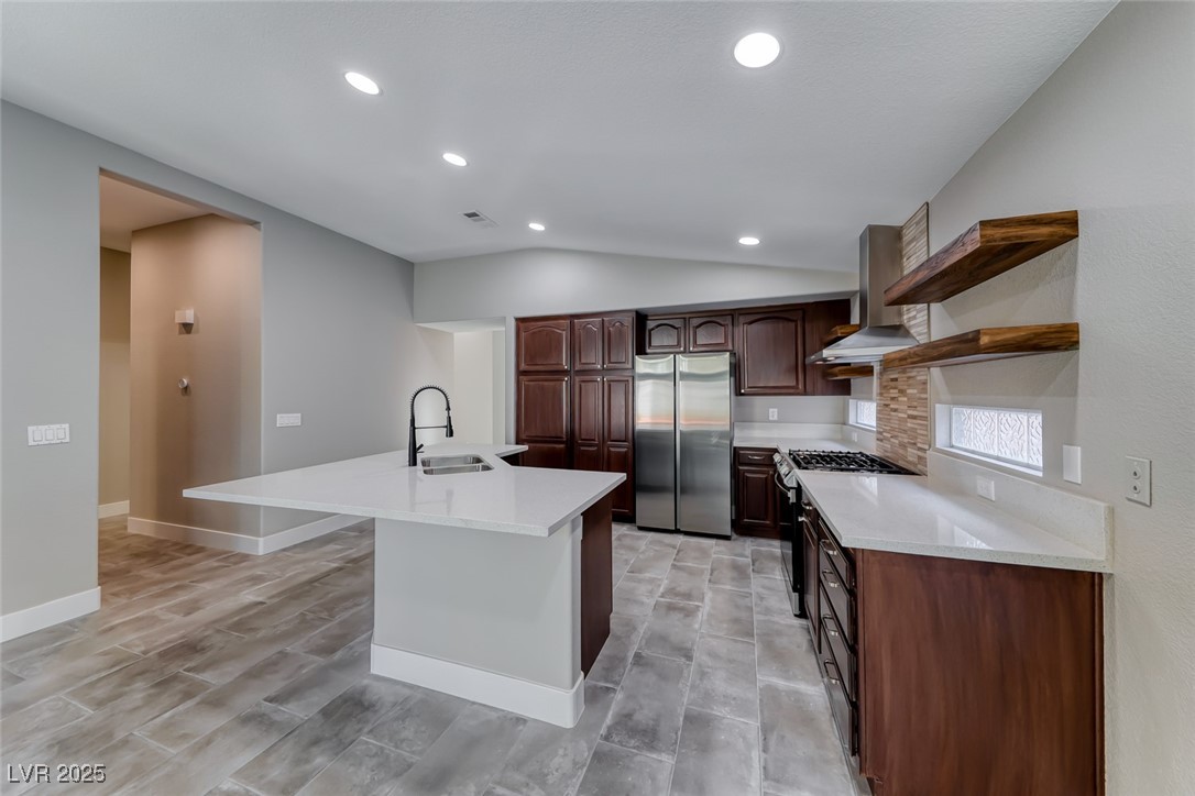 2401 Flower Spring Street Las Vegas, NV 89134 - Photo 21 of 42 Kitchen with open shelves, appliances with stainless steel finishes, wall chimney range hood, an island with sink, and light stone counters