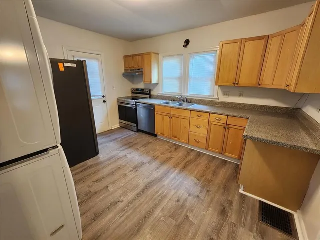 a kitchen with granite countertop wooden floors stainless steel appliances a sink and a refrigerator