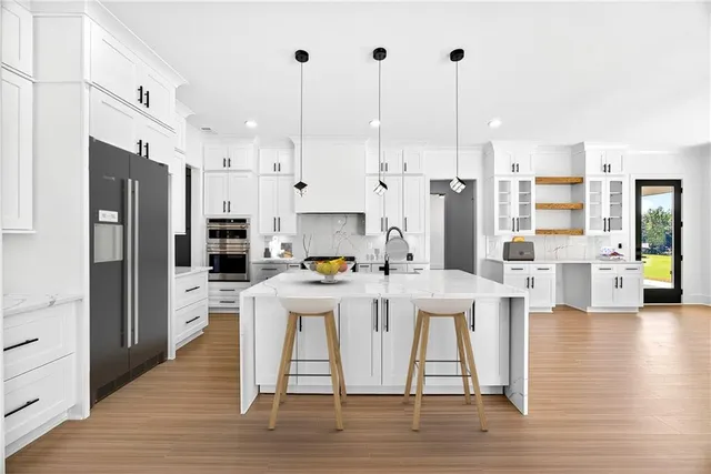 a kitchen with stainless steel appliances kitchen island granite countertop a refrigerator a stove a oven and white cabinets with wooden floor