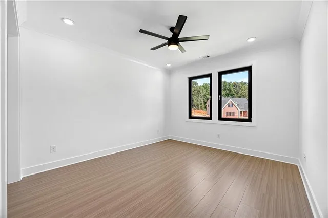 an empty room with wooden floor ceiling fan and windows