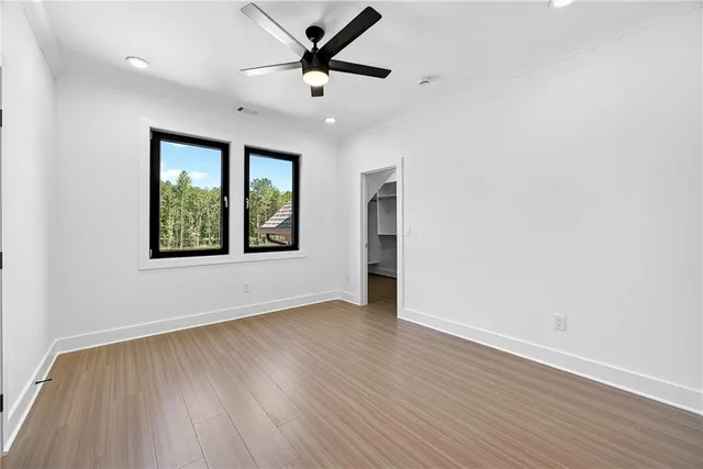an empty room with wooden floor ceiling fan and windows