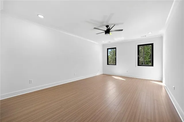 an empty room with wooden floor ceiling fan and windows