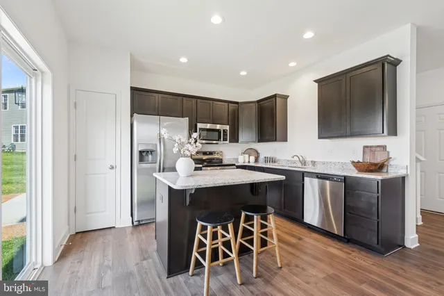 a kitchen with stainless steel appliances a sink a stove a refrigerator cabinets and a dining table with wooden floor