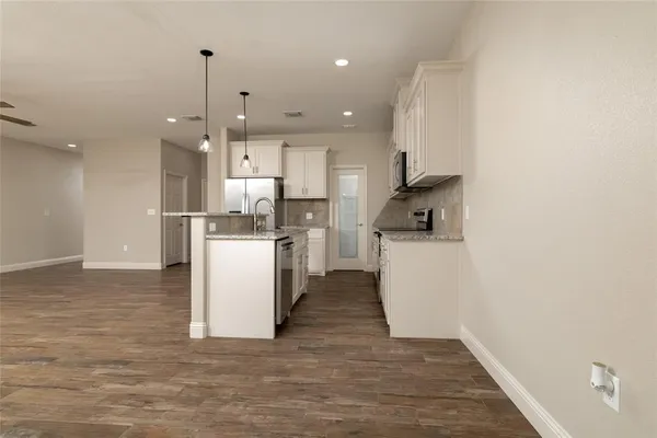 a kitchen with stainless steel appliances granite countertop a refrigerator a oven a sink and white cabinets with wooden floor