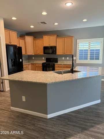an open kitchen with kitchen island a sink wooden floor and black appliances
