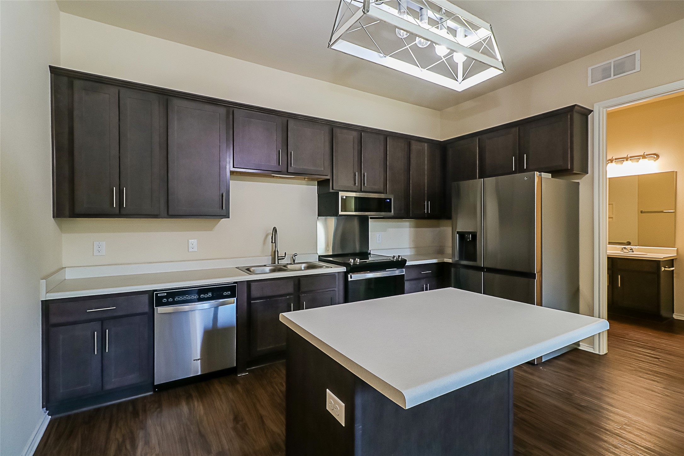 8601 West Gate Boulevard, Unit 7101 Austin, TX 78745 - Photo 8 of 16 Kitchen with dark wood finish cabinets, light countertops, stainless steel appliances, dark wood finished floors, and a center island