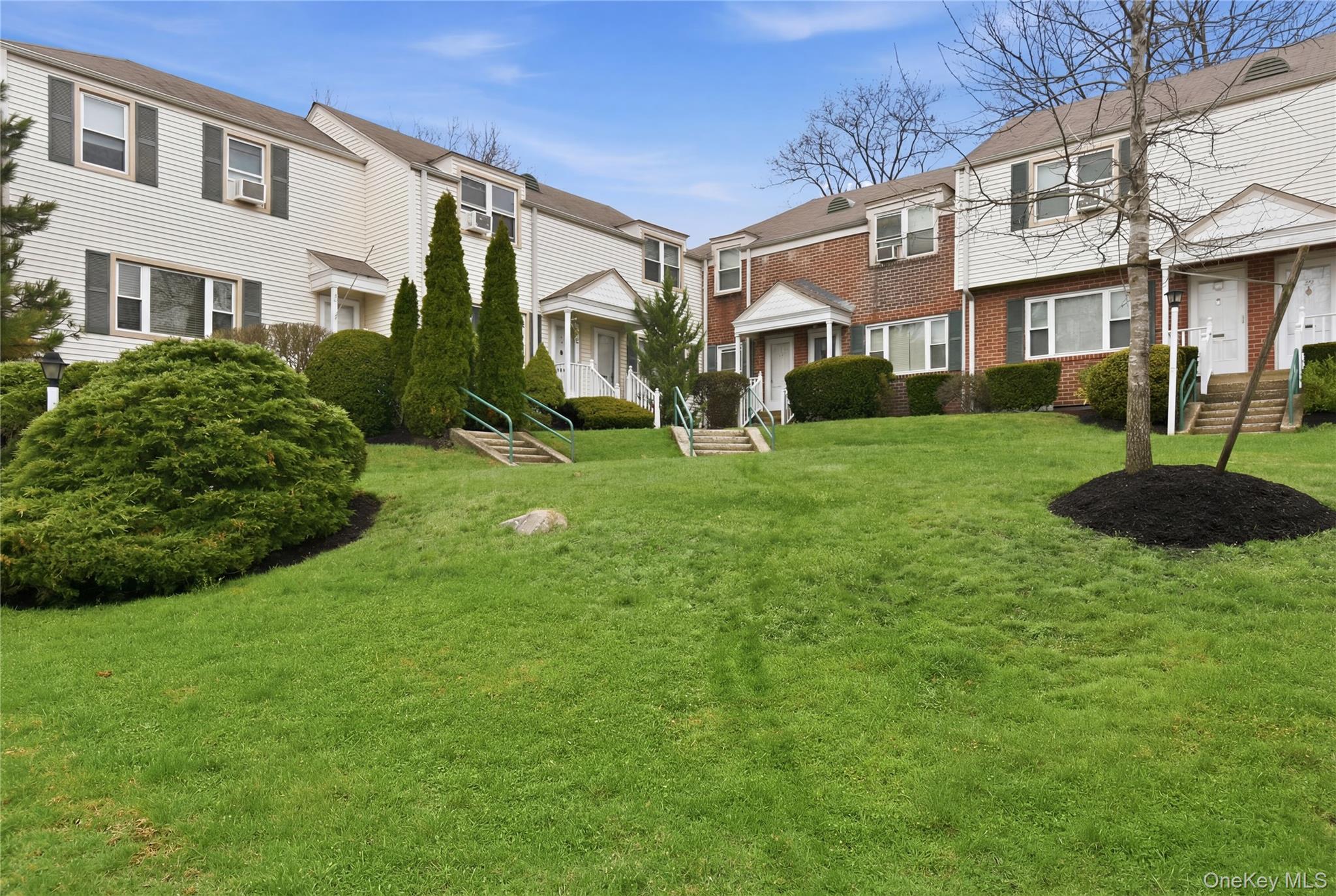 a view of a big yard in front of a brick house with a large tree