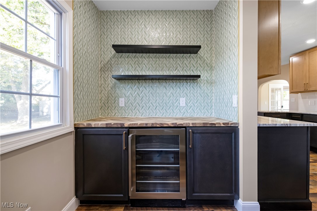 3716 Rolliston Road Cleveland, OH 44120 - Photo 19 of 37 Bar area featuring decorative backsplash, wine cooler, dark cabinets, open shelves, and plenty of natural light