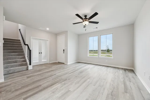 an empty room with wooden floor fan and windows