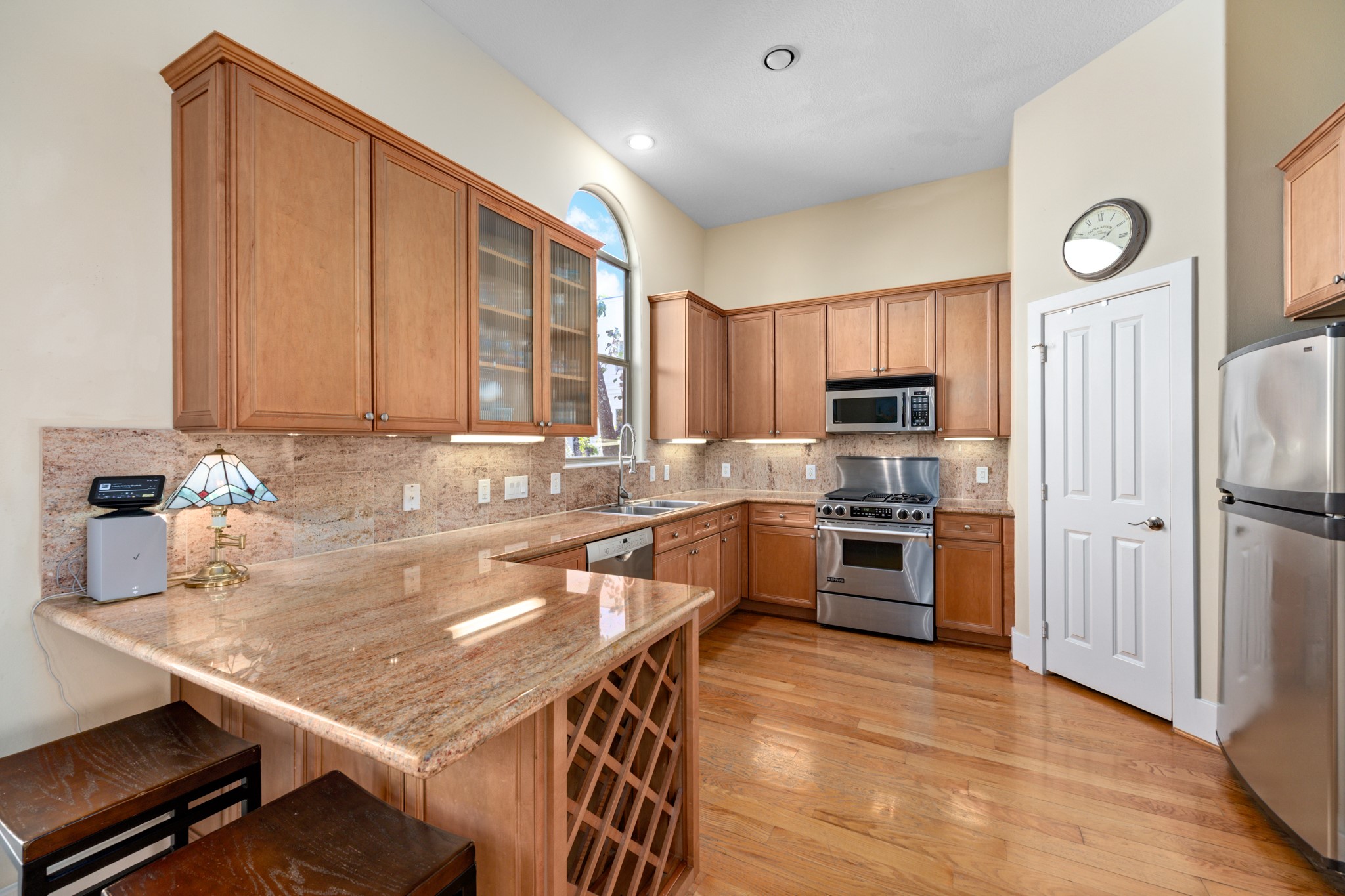 2611 Commonwealth Street Houston, TX 77006 - Photo 16 of 31 This kitchen features a warm, inviting design with warm wood cabinetry, granite countertops, and stainless steel appliances. A spacious peninsula provides additional prep space and casual seating. Tall ceilings and an arched window bring in abundant natural light, enhancing the open feel of the space. With ample storage, generous counter space, and thoughtful layout, this kitchen is well-suited for both entertaining and daily living.