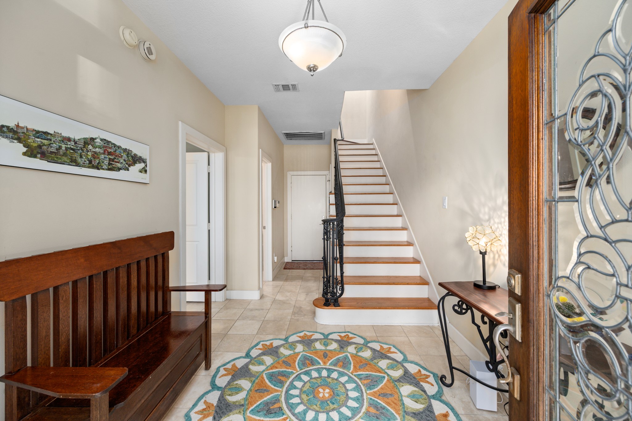 2611 Commonwealth Street Houston, TX 77006 - Photo 4 of 31 Welcoming front entry, featuring a bright, open foyer with tile flooring and a graceful staircase leading to the upper levels. The space is accented by warm wood details and elegant stair treads with wrought-iron railing. Natural light filters in through the decorative glass front door, creating an inviting first impression. Just off the entry, convenient interior access leads directly to the attached garage, offering everyday ease and functionality without sacrificing style.