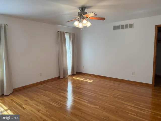 a view of an empty room with wooden floor and a chandelier fan