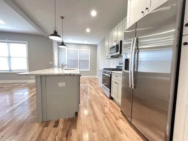 a kitchen with stainless steel appliances granite countertop a refrigerator a sink dishwasher a stove and white countertops with wooden floor