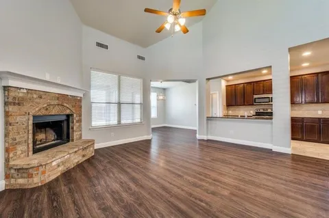 a view of a kitchen and an empty room with wooden floor a fireplace