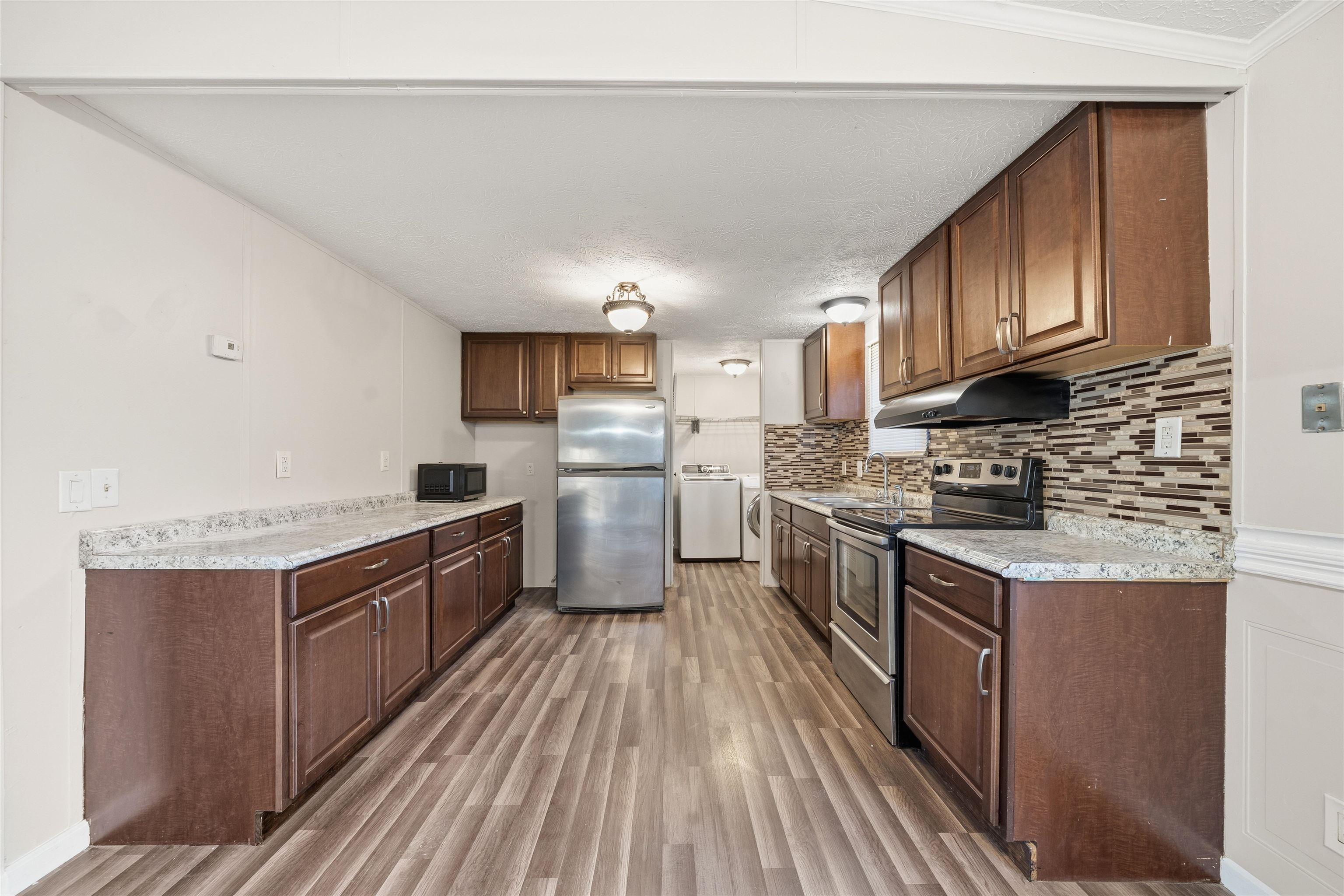 79 Stevens Road Mason, TN 38049 - Photo 7 of 21 Kitchen with stainless steel appliances, light wood-style floors, a textured ceiling, decorative backsplash, and under cabinet range hood
