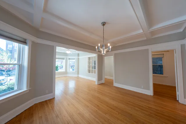 a view of an empty room with wooden floor kitchen view and a window