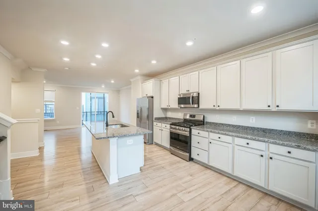 a large kitchen with stainless steel appliances granite countertop a stove a sink a refrigerator and white cabinets with wooden floor