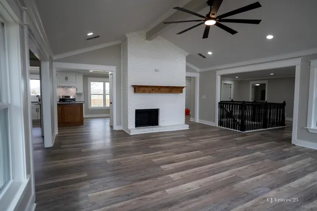 a view of a livingroom with a fireplace a ceiling fan wooden floor and kitchen space