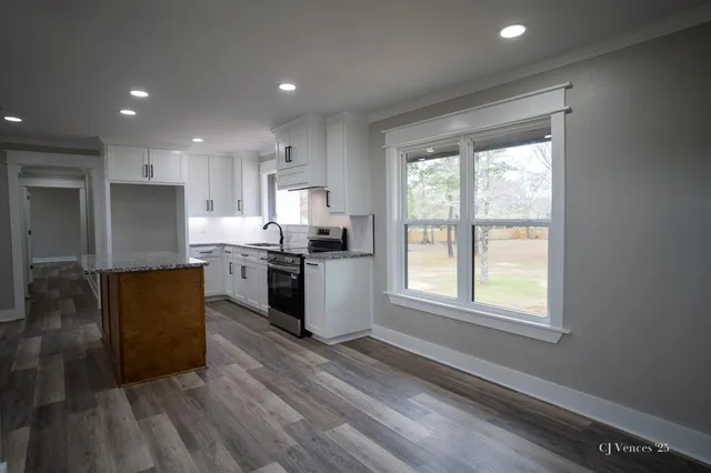 a kitchen with stainless steel appliances granite countertop a refrigerator a sink dishwasher a stove and white countertops with wooden floor