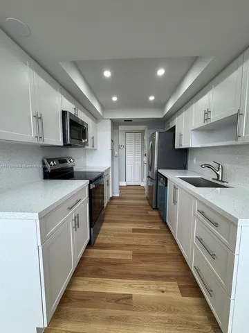 a large kitchen with stainless steel appliances granite countertop a sink a stove top oven and white cabinets