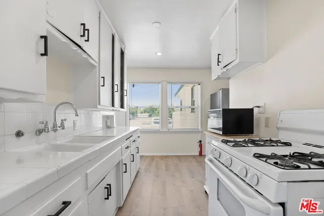 a kitchen with a stove a sink and a flat screen tv