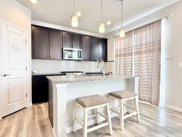 a kitchen with stainless steel appliances granite countertop a stove a sink a microwave a refrigerator and white cabinets with wooden floor