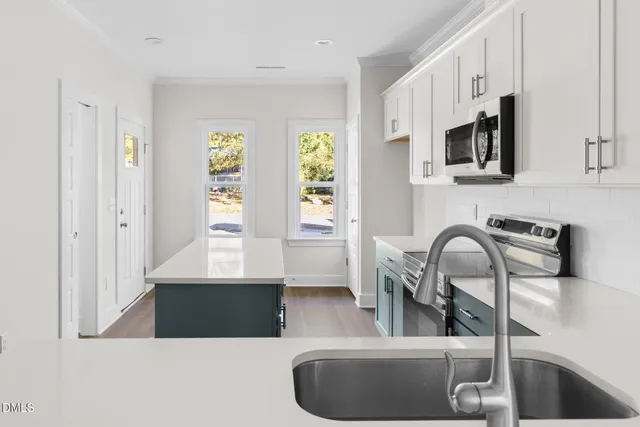 a kitchen with stainless steel appliances a sink a microwave a stove and white cabinets with wooden floor