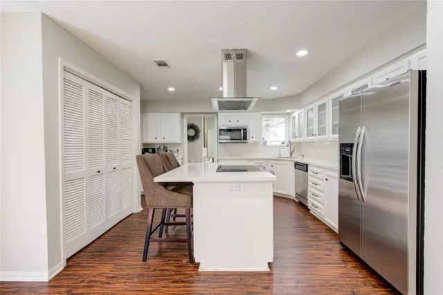 a kitchen with stainless steel appliances a refrigerator a stove microwave and white cabinets with wooden floor