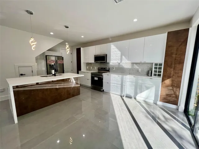 a large kitchen with stainless steel appliances granite countertop a large counter top a stove a sink a refrigerator white cabinets and a granite counter tops