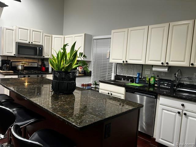 89 Muir Road Grosse Pointe, MI 48236 - Photo 17 of 29 Kitchen featuring granite countertops, white cabinetry with dark hardware, stainless steel appliances, and an island with seating