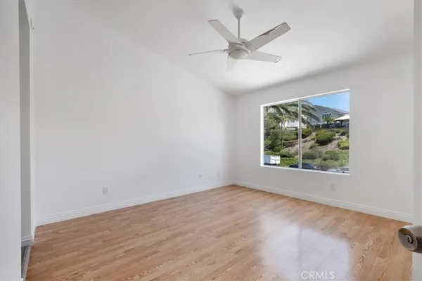 an empty room with wooden floor ceiling fan and window