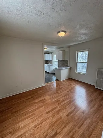 an empty room with wooden floor kitchen view and windows