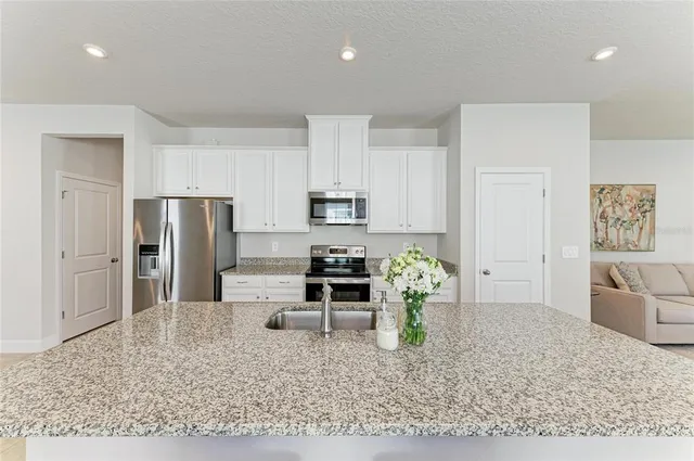 a kitchen with stainless steel appliances a stove a sink a microwave a refrigerator white cabinets and couches with wooden floor