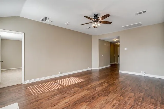 a view of an empty room with wooden floor and a ceiling fan
