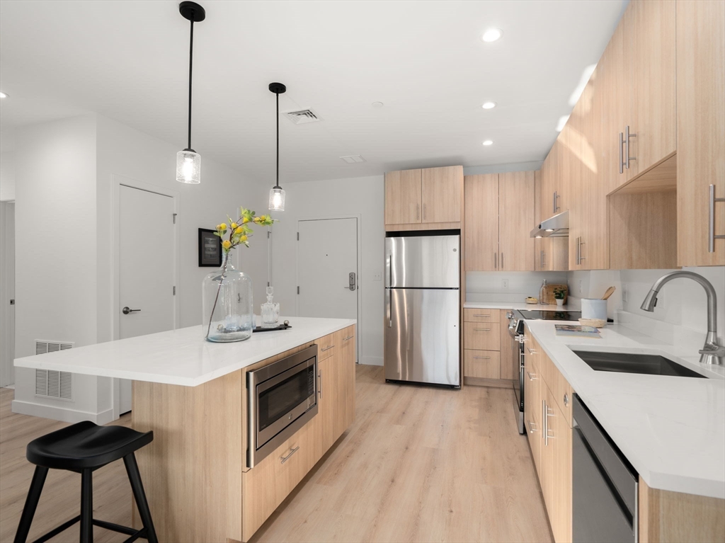 1151 Walnut Street, Unit 406 Newton, MA 02461 - Photo 7 of 32 a kitchen that has a sink a center island stainless steel appliances and cabinets