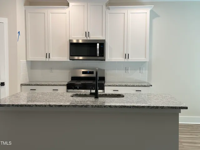 a kitchen with granite countertop a sink a stove and white cabinets