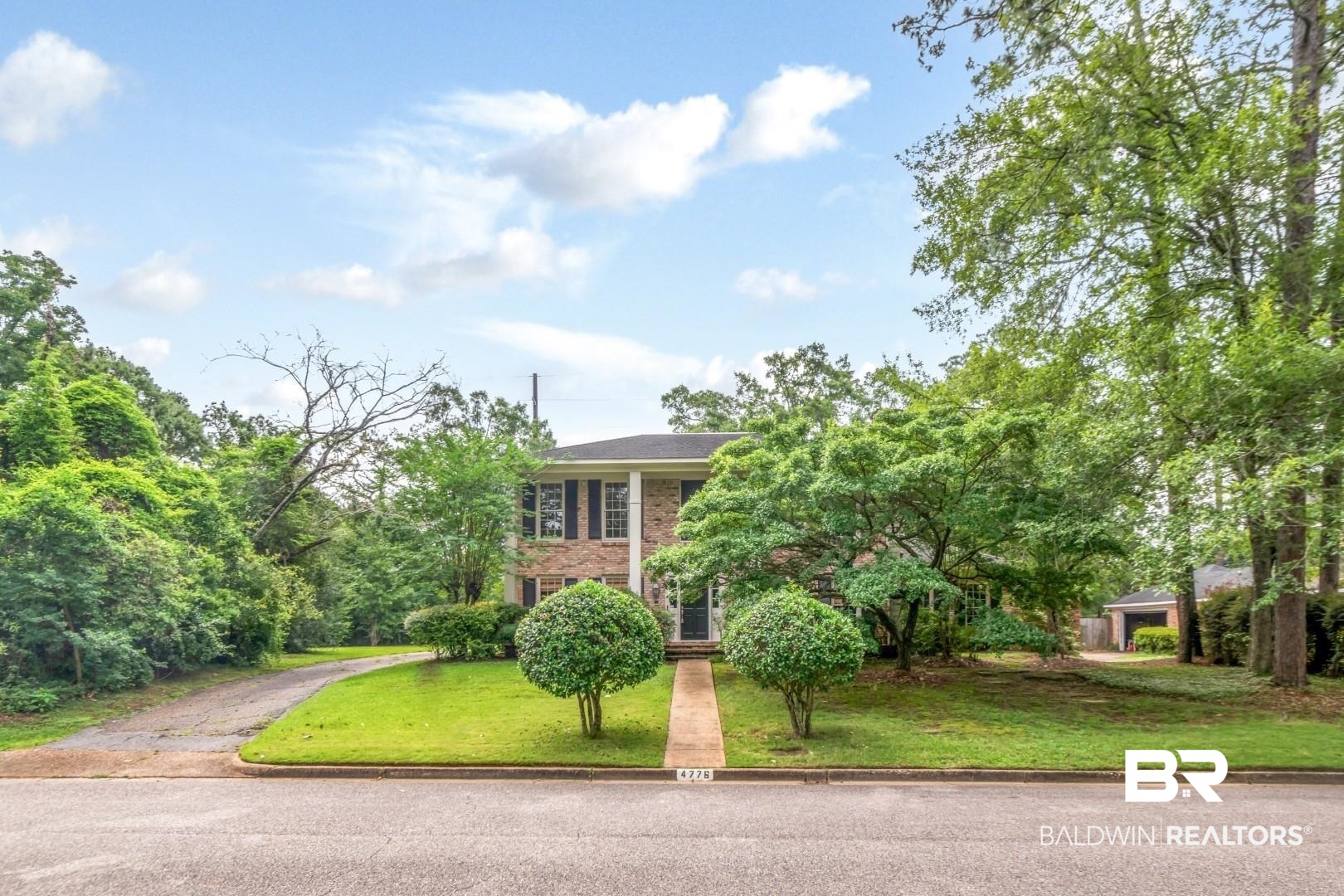 4776 Falls Church Road Mobile, AL 36608 - Photo 41 of 45 Brick facade residence featuring a front lawn with manicured shrubs, mature trees, a paved driveway, and a concrete walkway to the entrance