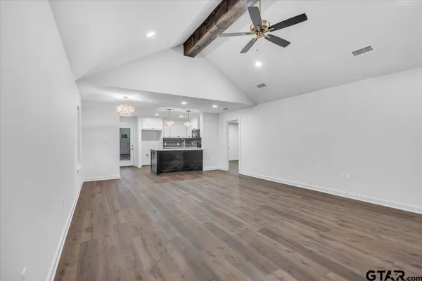 an empty room with wooden floor ceiling fan and kitchen view