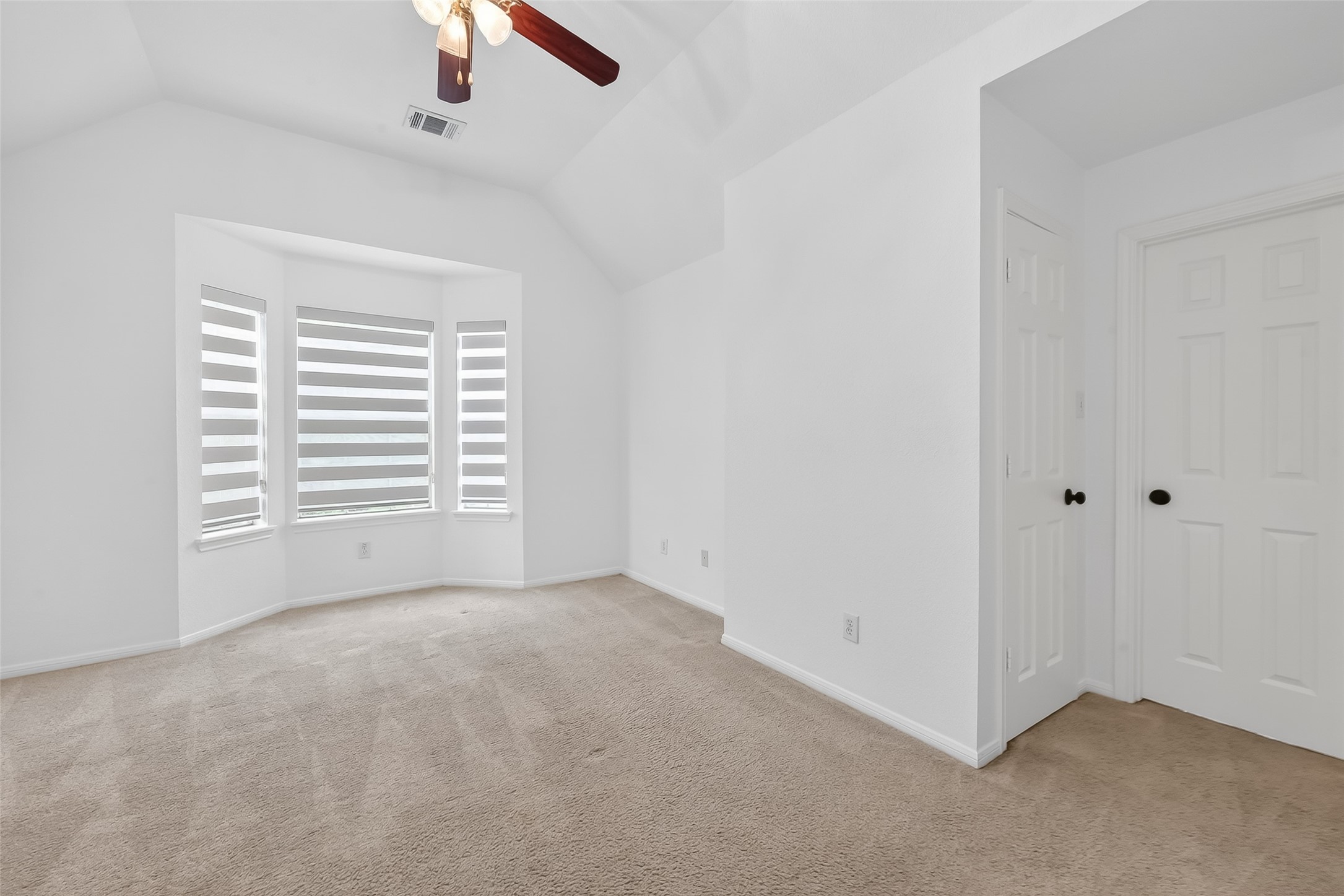 1311 Rene Court Sugar Land, TX 77479 - Photo 32 of 45 Bright, spacious room with neutral carpet and walls. Features a large bay window with modern blinds, ceiling fan, and two white doors. Ideal for a bedroom or office space.