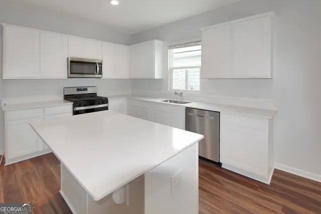 a kitchen with stainless steel appliances a stove a sink a microwave a refrigerator white cabinets and wooden floor