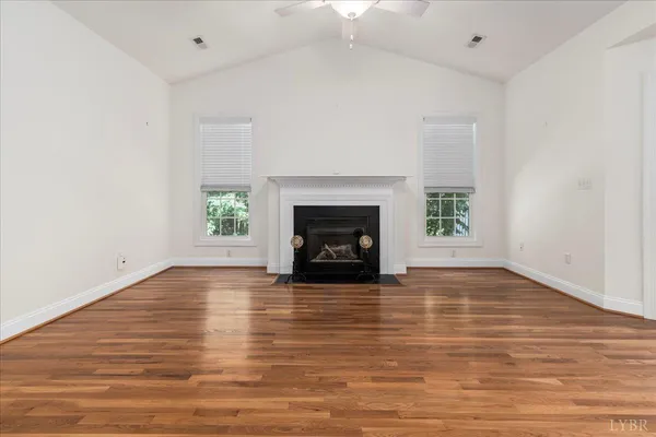 a view of an empty room with wooden floor fireplace and a window