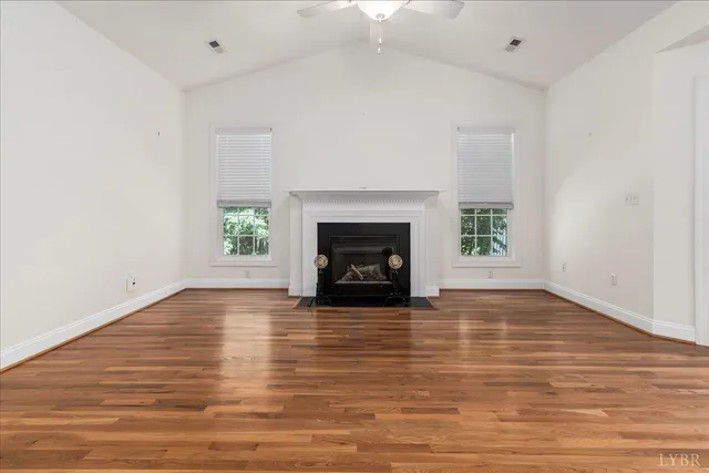 a view of an empty room with wooden floor fireplace and a window
