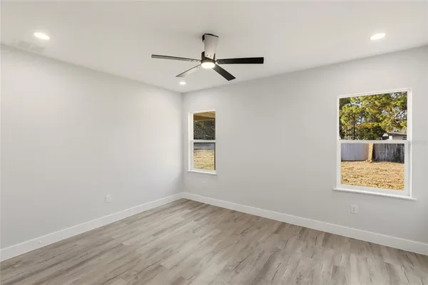 an empty room with wooden floor ceiling fan and windows