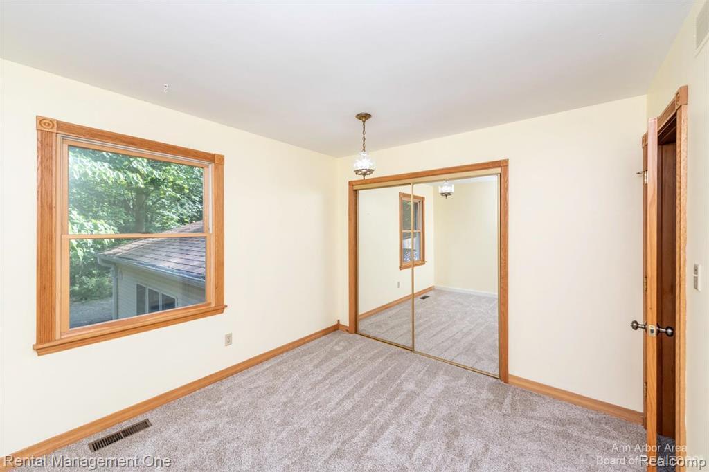 7870 Chamberlin Road Dexter, MI 48130 - Photo 31 of 52 Carpeted room featuring a double-paned window with wood trim, mirrored closet doors, and wood-finish door frames