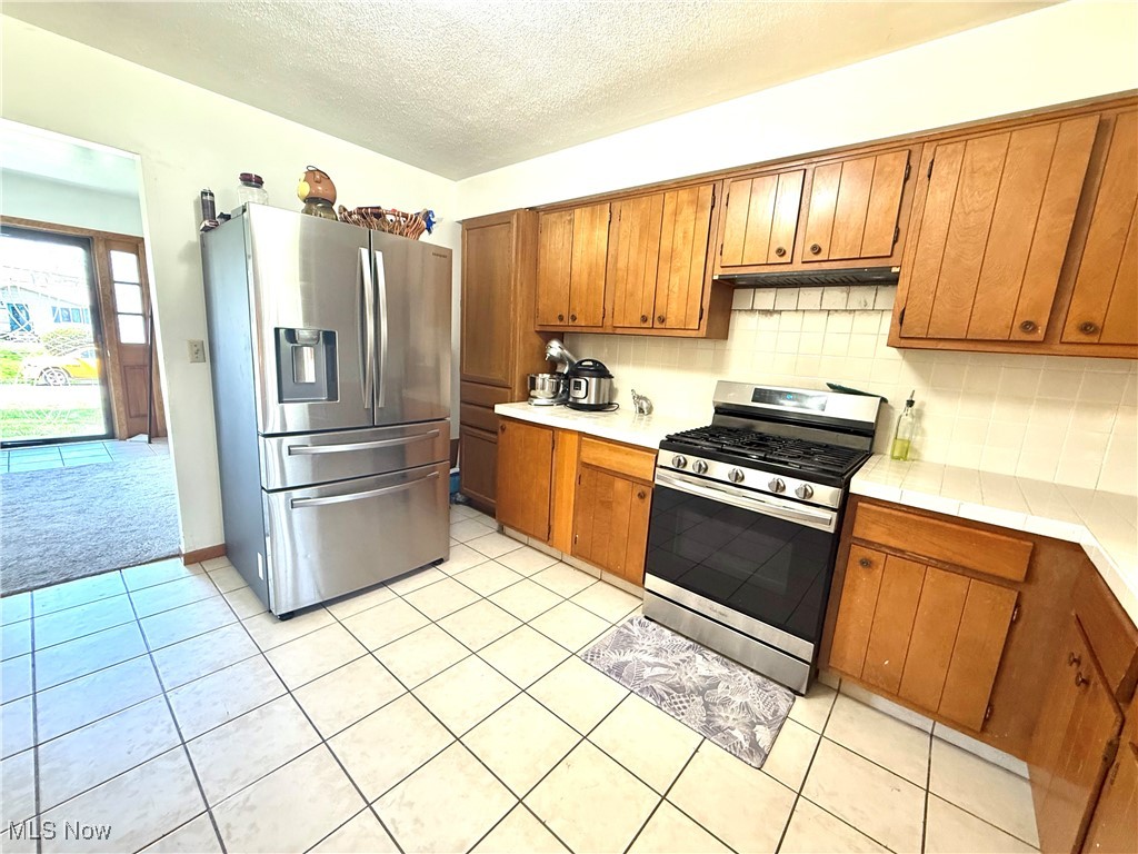 4669 Mars Road Uniontown, OH 44685 - Photo 15 of 31 Kitchen featuring tasteful backsplash, brown cabinets, a textured ceiling, and light tile patterned flooring