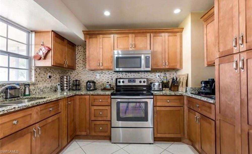 5325 23rd Place Southwest Naples, FL 34116 - Photo 3 of 10 Kitchen featuring wood cabinetry, stainless steel appliances, speckled stone countertops, a tiled backsplash, and recessed lighting